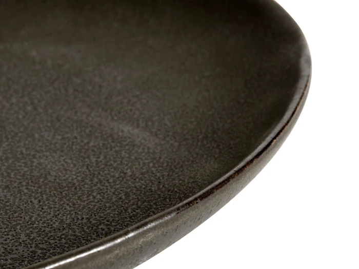 Nærbillede af kanten på en mørk, struktureret keramiktallerken med en glat, let skinnende overflade og en afrundet kant.