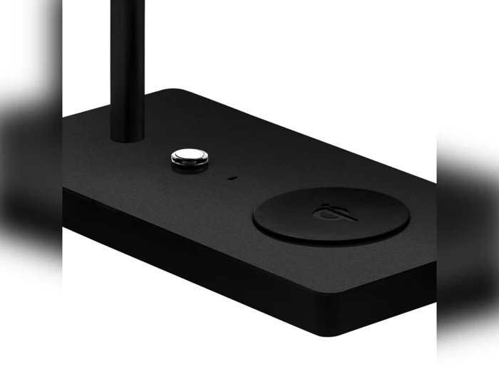 Et nærbillede af en sort rektangulær opladningsdock med en rund trådløs opladningsplade og en lille knap på overfladen.