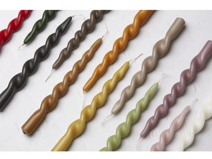 Farverige snoede lys i forskellige nuancer, arrangeret diagonalt på en hvid struktureret overflade. Hvert lys har et spiraldesign og en synlig væge.