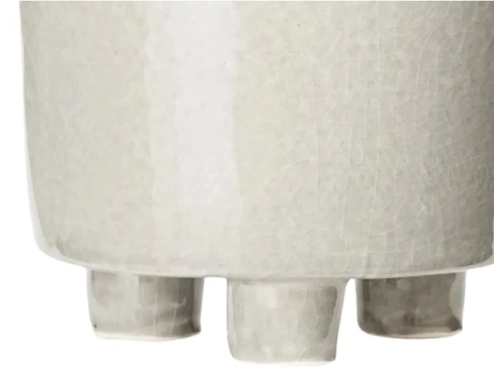 Nærbillede af et lysegråt, struktureret keramikkar med tre afrundede ben i bunden.