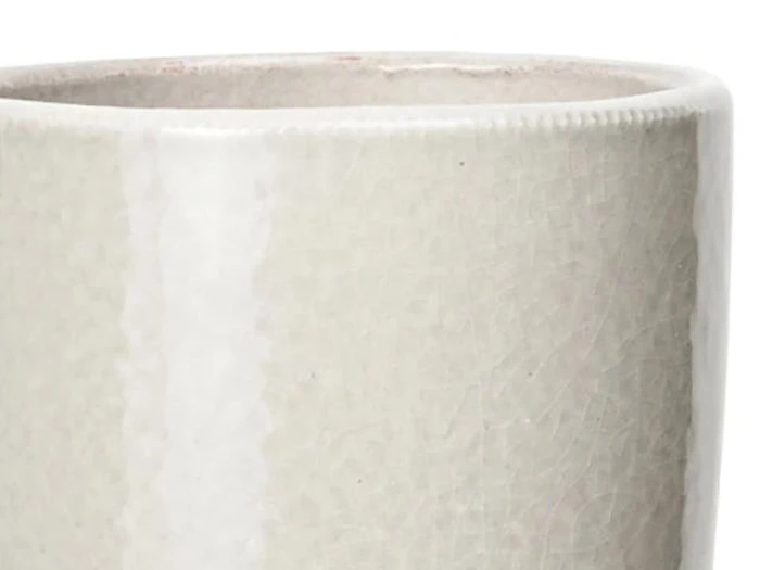 Nærbillede af kanten og den øverste del af et struktureret, råhvidt keramikkrus med en lodret stribe og en lidt ujævn, organisk kant.