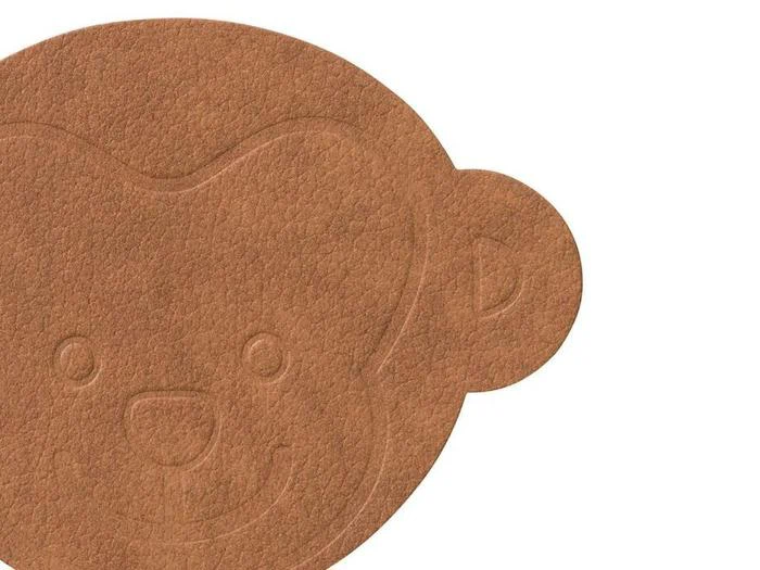 En brun, struktureret bordskåner formet som et abeansigt med enkle, prægede ansigtstræk og et synligt øre.