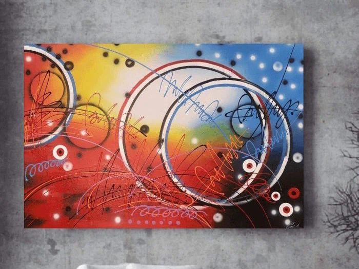 Abstrakt maleri med levende røde, gule, blå og hvide områder, gennemskåret af sorte og hvide cirkler, linjer og skriblerier på en struktureret grå væg.