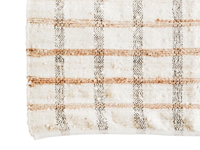 Et nærbillede af et beige vævet stof med et ternet mønster af brune og mørke linjer, der viser strukturerede fibre og let flossede kanter.