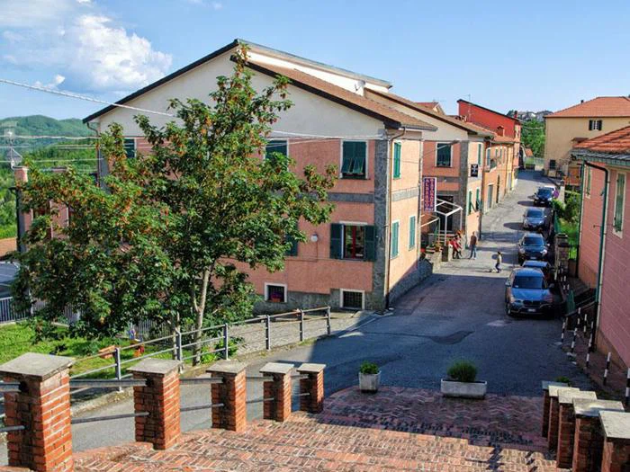 En murstenstrappe fører ned til en smal gade med parkerede biler, farverige bygninger og et grønt træ under en blå himmel.