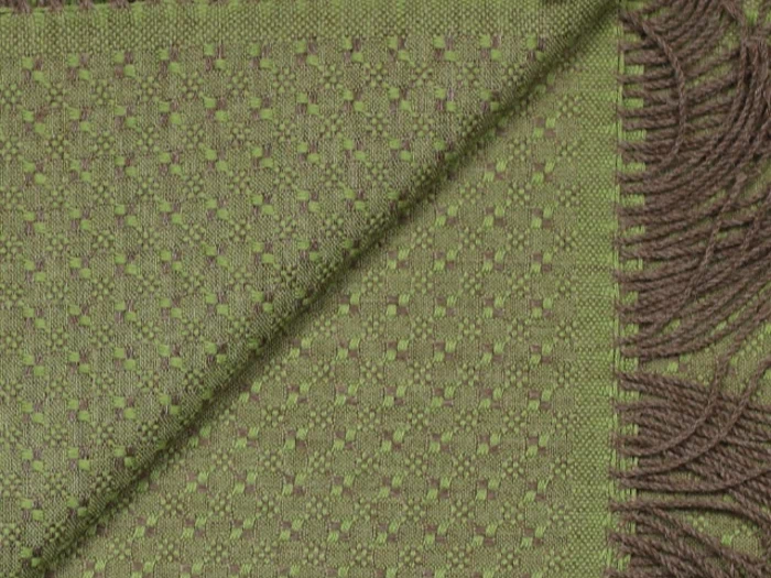 Et nærbillede af et grønt vævet tekstil med et lille firkantet mønster, foldet diagonalt, og brune frynser langs den ene kant.
