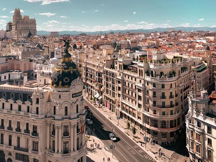 Luftfoto af Madrid med den udsmykkede Metropolis-bygning, travle gader, klassisk arkitektur og fjerne bjerge under en klar himmel.