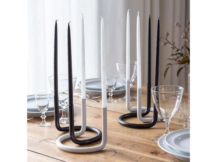 Et spisebord i træ med tallerkener, glas og moderne sort-hvide spiralformede lysestager med høje sort-hvide stearinlys.