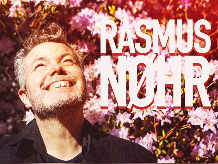 En smilende mand kigger op foran blomstrende pink blomster, med fed tekst RASMUS NØHR ved siden af ham.
