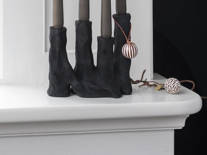 Tre sorte lysestager i en hvid vindueskarm med to stribede brune og hvide ornamenter, et hængende og et hvilende i nærheden.