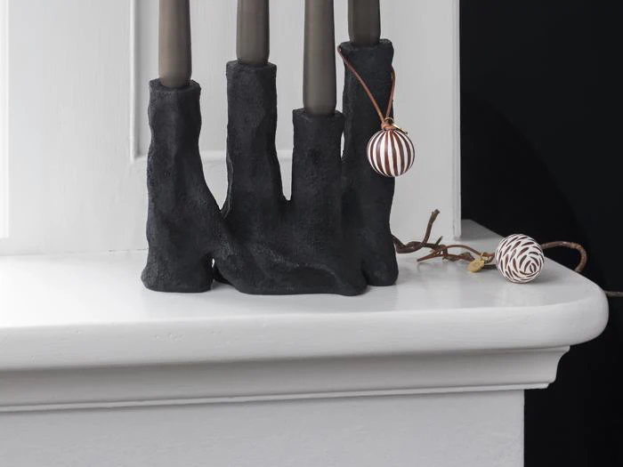 Tre sorte lysestager i en hvid vindueskarm med to stribede brune og hvide ornamenter, et hængende og et hvilende i nærheden.