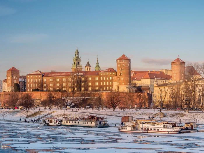 Wawel-slottet i Kraków, Polen, har udsigt over en delvist frossen flod om vinteren med både, der ligger ved den iskolde bred, og sne, der dækker jorden.
