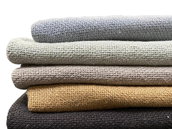 En stak med fem foldede strikkede trøjer i dæmpede farver: lyseblå, lysegrøn, beige, sennepsgul og mørkebrun på en hvid baggrund.