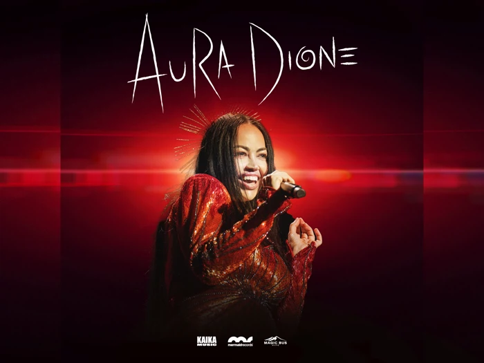 En kvinde i funklende rødt tøj synger i en mikrofon på scenen, og over hende står der Aura Dione med store hvide bogstaver på en rød baggrund.