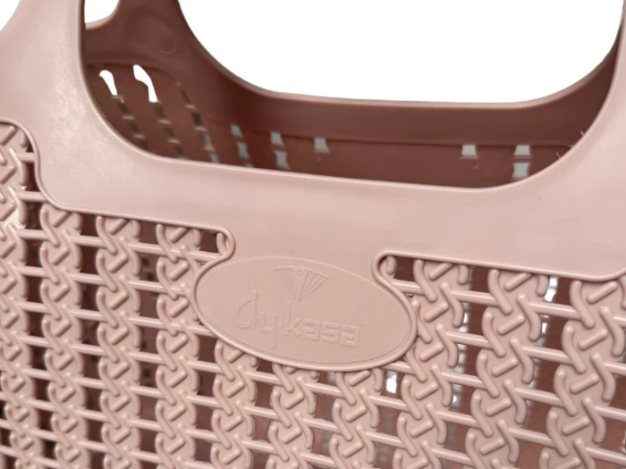 Nærbillede af en lyserød plastkurv med vævet tekstur og et præget logo i midten.