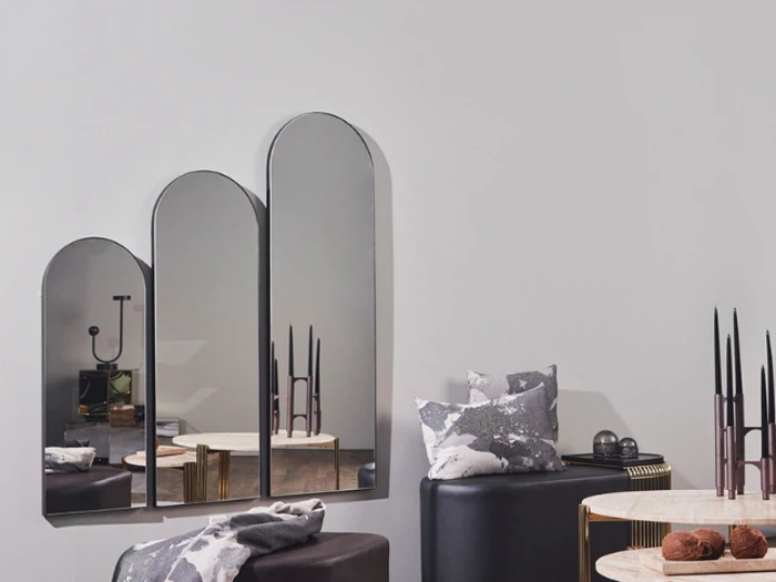 Et moderne opholdsrum med tre buede spejle på en lys væg, et rundt bord, stearinlys og mønstrede puder på sorte siddepladser.