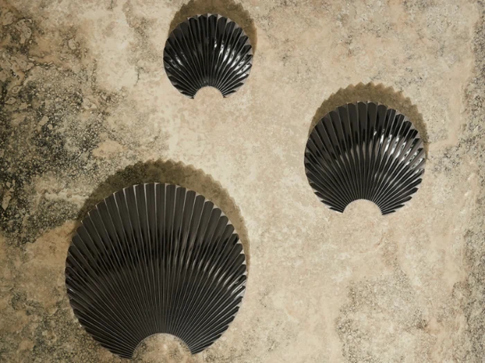 Tre sorte vifteformede vægskulpturer er monteret på en struktureret beige og grå væg, arrangeret i et løst trekantet mønster.