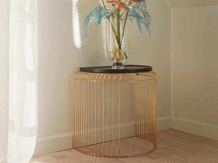 Et moderne sidebord med sort plade og guldtrådsfod står i et hjørne med en glasvase med pastelfarvede blomster og blade.