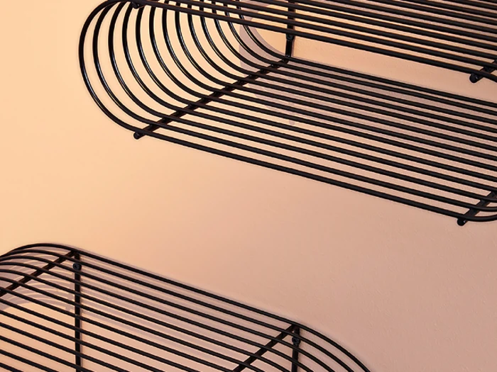 Nærbillede af tre væghylder i sort metaltråd monteret på en beige væg, med buede kanter og vandrette stænger.