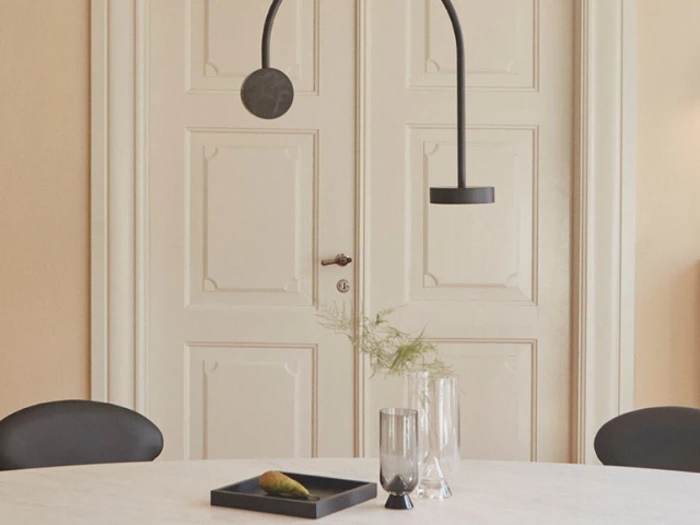 Minimalistisk spiseplads med et hvidt bord, sorte stole, moderne sorte pendler, glasvaser, en bakke og dobbelte cremefarvede paneldøre i baggrunden.