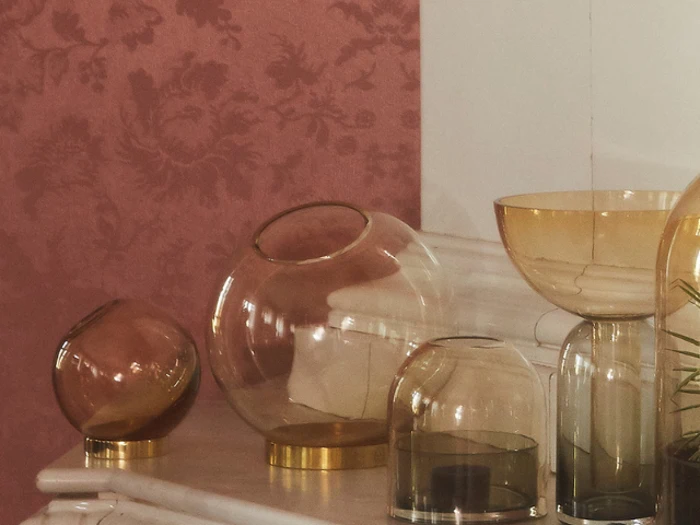 Glasvaser og skåle i forskellige størrelser står på en hvid marmoroverflade mod en struktureret, pink og rød blomstret tapetbaggrund.