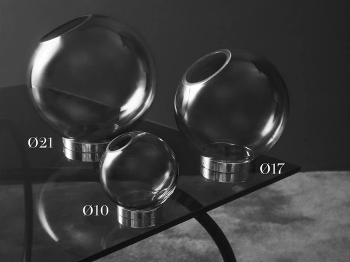 Tre glaskugler med vinklede åbninger og metalbunde, mærket Ø21, Ø17 og Ø10, er udstillet på et glasbord mod en mørk baggrund.