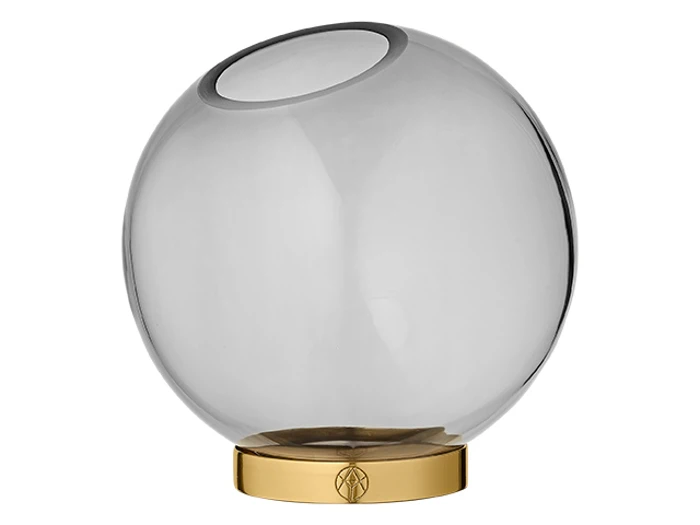 En rund, gennemsigtig glasvase med skrå åbning står på en skinnende, guldfarvet cirkulær base.