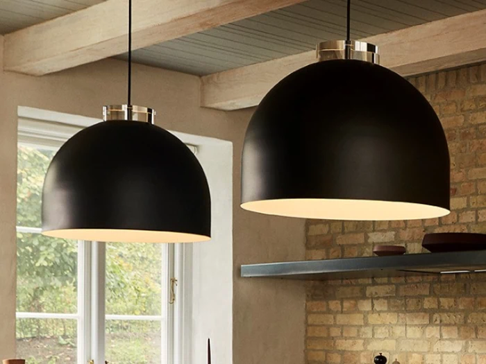 To store, sorte kuppelformede pendler hænger fra loftet i et hyggeligt rum med murstensvægge og et vindue, der lukker naturligt lys ind.