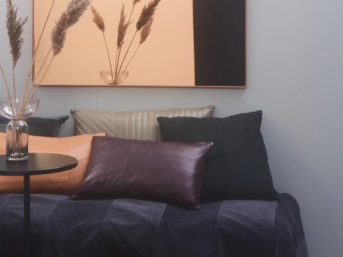 Et hyggeligt siddeområde med forskellige puder, et rundt sidebord, vaser med tørret pampasgræs og et moderne abstrakt maleri på væggen bagved.