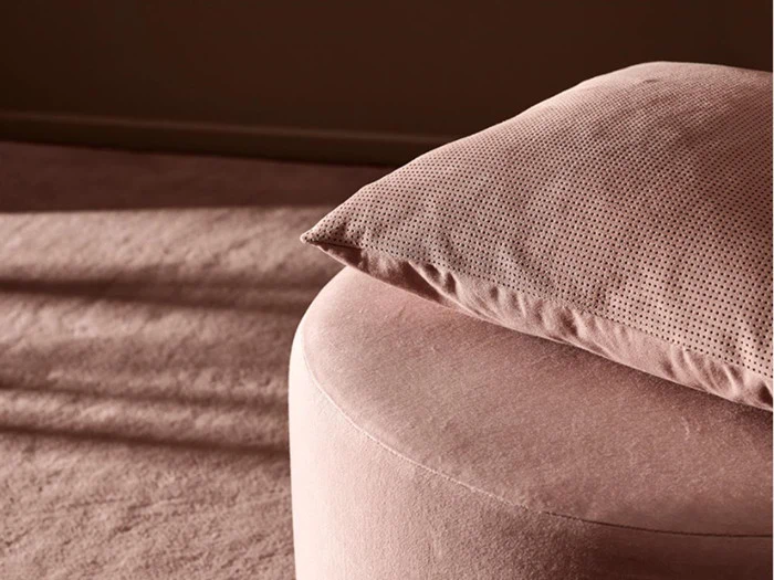Et nærbillede af en blød, lyserød pude, der hviler på en rund, lyserød skammel i et varmt oplyst rum med matchende gulvtæppe.