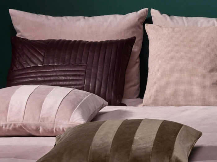 Fire pyntepuder i rosa, brune og beige nuancer er anbragt på en seng med en grøn væg i baggrunden.