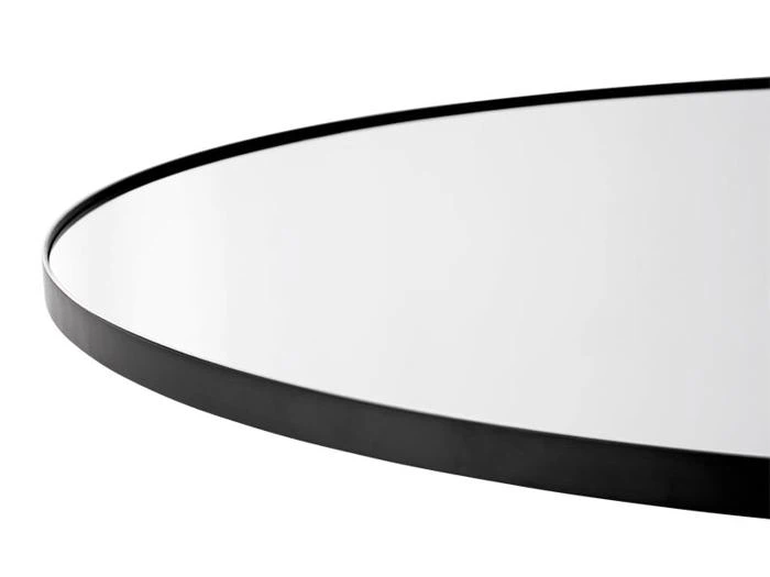 Nærbillede af kanten af et rundt spejl med en tynd, sort metalramme mod en hvid baggrund.