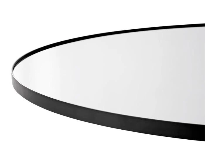 Et nærbillede af et rundt spejl med en tynd sort ramme, fotograferet mod en hvid baggrund.