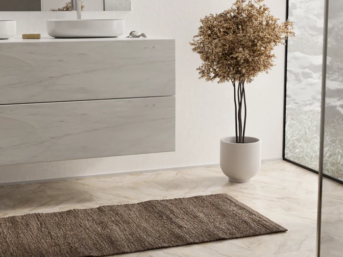 Moderne badeværelse med håndvask i lyst træ, hvid karvask, brun gulvmåtte, potteplante og stort vindue, der lukker naturligt lys ind.