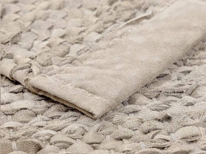 Nærbillede af et struktureret beige vævet tæppe med et foldet hjørne, der viser dets tykke, flettede konstruktion og bløde stofmateriale.