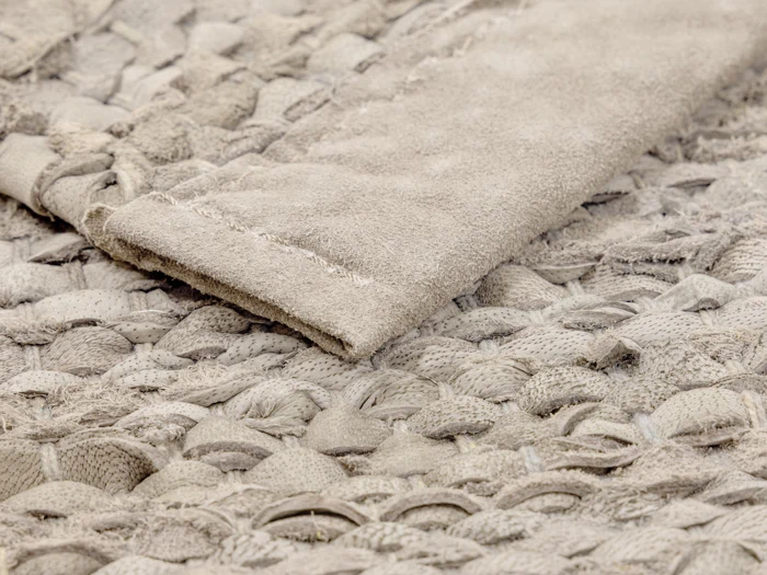 Et nærbillede af et beige vævet stof med en foldet kant, der viser detaljeret tekstur og syninger.