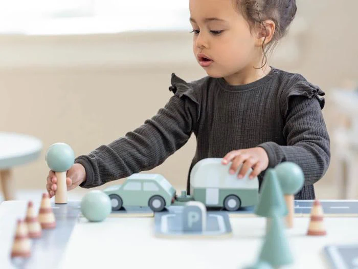 Et lille barn leger med legetøjsbiler, træer og kegler på et lille bylegesæt på en bordplade og fokuserer intenst på at arrangere delene.