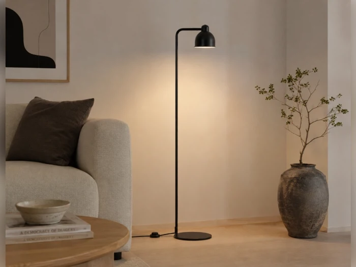 En slank, sort gulvlampe, der står mellem en sofa og en stor dekorativ vase.