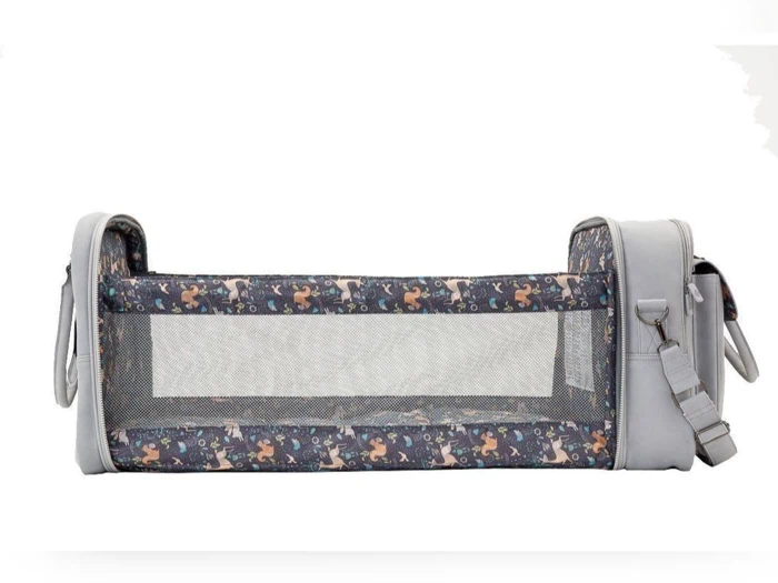 En bærbar grå vugge med netsider, dyremønstret kant og påsatte poser i begge ender, vist på en hvid baggrund.