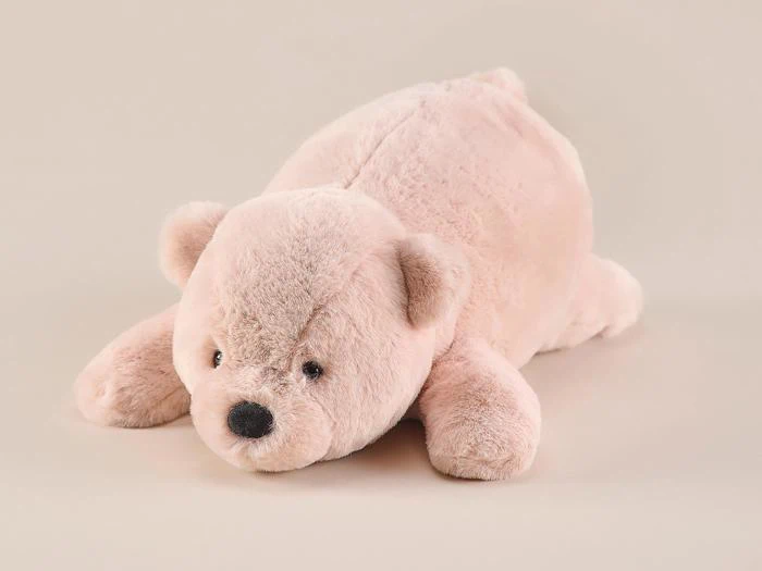 En blød, lyserød plysbamse, der ligger fladt på maven mod en almindelig beige baggrund.