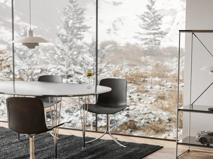 Moderne spiseplads med rundt bord, tre sorte stole, et glas hvidvin og et stort vindue med udsigt til snedækkede træer og landskabet udenfor.