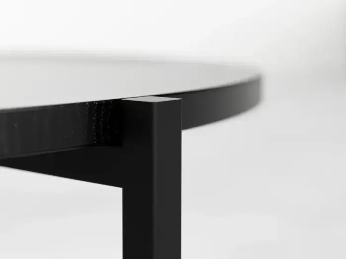 Nærbillede af kanten og benet på et moderne sort metal- og træbord på en almindelig, lys baggrund.