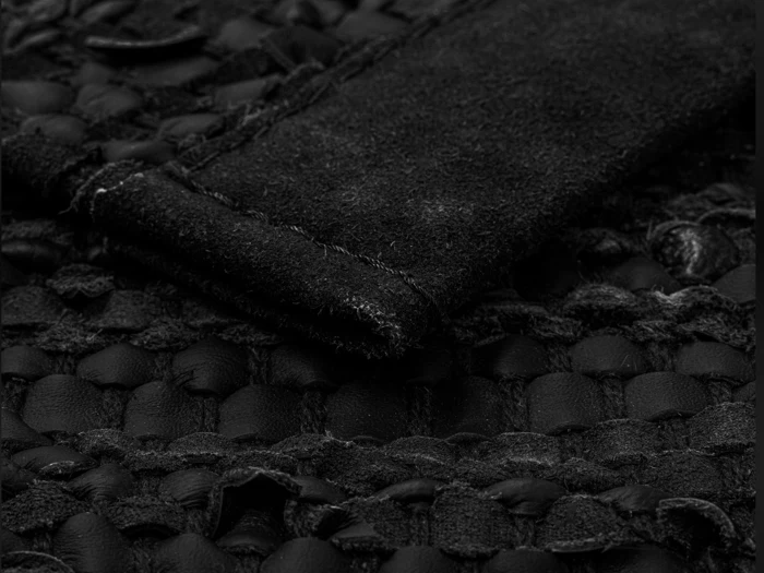 Et nærbillede af vævet sort læder og ruskind med synlige syninger og lagdelt materiale.