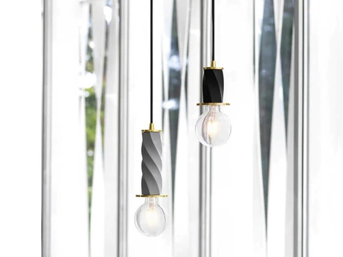 To moderne pendler med armaturer i sort og guld hænger foran et vindue med geometriske paneler i matteret glas.