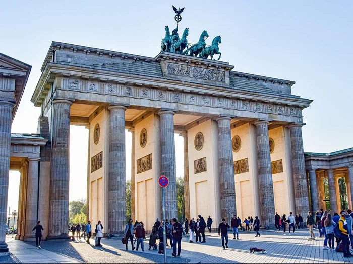 Brandenburger Tor i Berlin, Tyskland, med mennesker, der går og samles omkring søjlerne på en solrig dag.