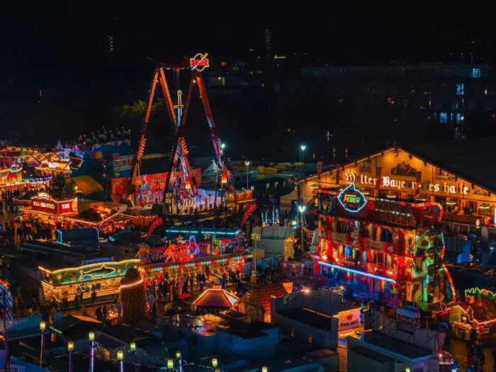 En livlig nattescene på et tivoli med stærke, farverige lys, forlystelser og overfyldte boder, der skaber en festlig atmosfære.