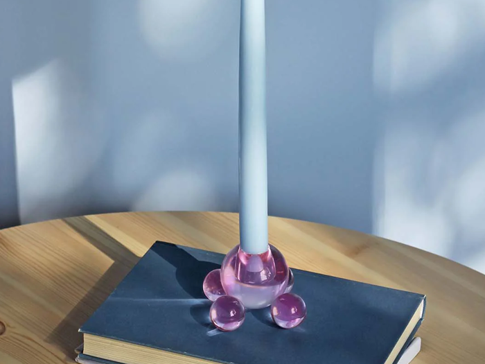 Et blåt stearinlys i en lyserød glasholder står på en lukket hardcover-bog på et træbord med blødt lys og skygger i baggrunden.