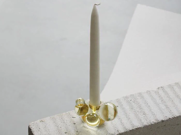 Et hvidt bloklys står i en glasholder med flere klare, runde bobler, placeret på en struktureret hvid overflade.