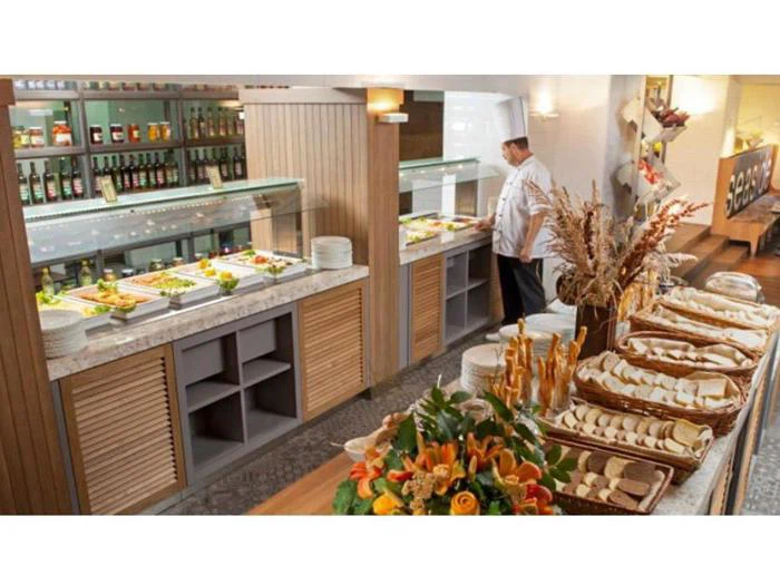 En kok står ved en buffet med salater, brød, olier og forskellige retter arrangeret på diske i et lyst, moderne restaurantmiljø.