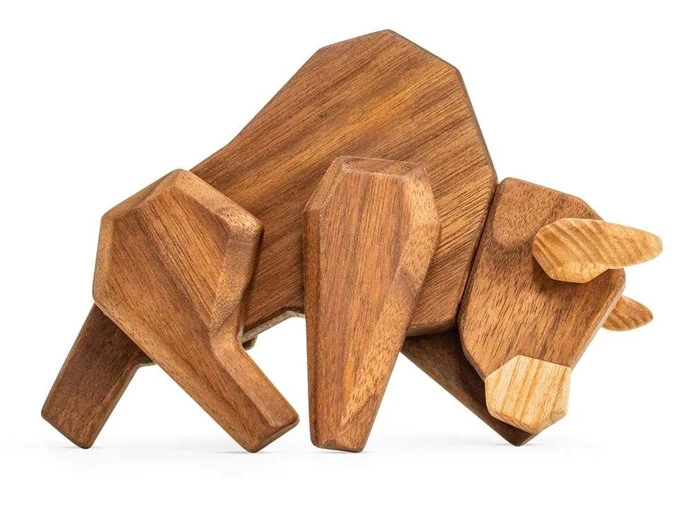 En geometrisk træskulptur af en tyr med kantede former og en glat finish, der står på en hvid baggrund.